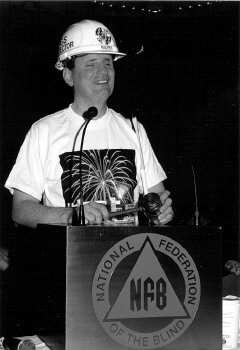 President Maurer, wearing his T-shirt and hard hat, returns to the podium.