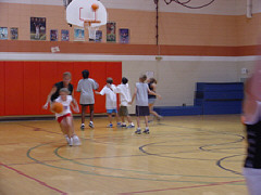 In the gym students dribble and make baskets using all five basketball nets.