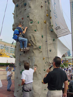 David Venet halfway up the climbing wall with Erik Weihenmayer and Gerry Sandusky standing at the bottom lookin gon.