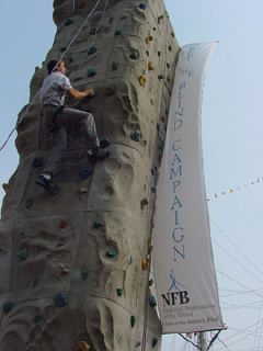 Erik Weihenmayer is halfway up the climbing wall.  The huge Meet-the-Blind banner can be seen stretching down from the top of the wall.