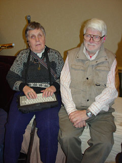 A couple are seated, but not on chairs.   The woman has an electronic notetaker in her lap.