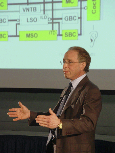 Pictured here is Ray Kurzweil gesturing at a complicated graphic visible on the screen behind him.