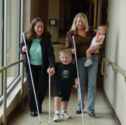 Left to right Angela Wolf, Lance Roberts, and Brenda Dunn, carrying Lance�s little sister, walk down the hall at the Texas convention. Angela is showing Lance how to hold and use his cane.
