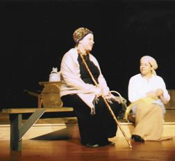 Gail Snider as Yente in Fiddler on the Roof sits on a bench wearing a wedding shawl that she made herself using a nineteenth century pattern that she found while doing research on the Internet.