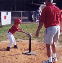 Ryan hits the ball while his dad cheers him on.