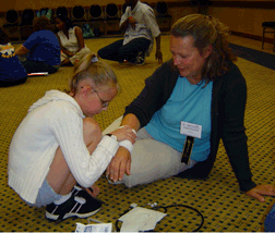 Mother sits patiently as her daughter practices bandaging a fictitious wound on ther forearm.
