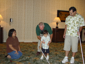Elizabeth Valois sits and Fernando Valois looks on from the right, while 4-year-old son Tomas Valois learns cane travel techniques with instructor Brian Schetele at the 2006 NFB convention.