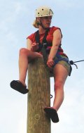 A mentor sits on top of a pole during a ropes course activity.