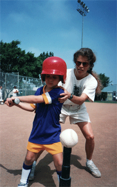 Mom helps Kyra (age 6) get into batting position for a T-ball game.