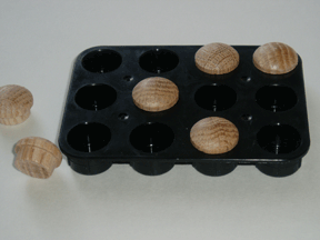 The plastic base normally secures glue sticks, but in this case can represent two Braille cells side-by-side. Oak �buttons� are placed strategically to represent the Braille code. Here, the word �mother� is represented.