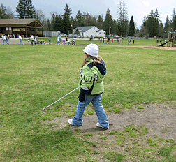 Not all cane travel is urban. Here a young girl crosses the open lawn of a playground and uses environmental clues in order to find her way back to the classroom. 
