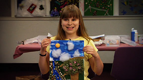 Blind student proudly holds up her artwork.