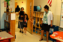 Her teachers, Ms. Peggy Echt and Ms. Mary Kaye Moore, look on while Kendra, with cane in hand, enters the classroom on her birthday. 