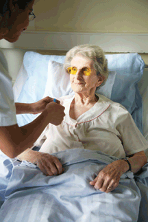 A woman sits up in a hospital bed as her nurse leans over her.
