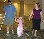 Young blind girl with a cane while her sighted father, under sleepshades and with cane, walks along beside her