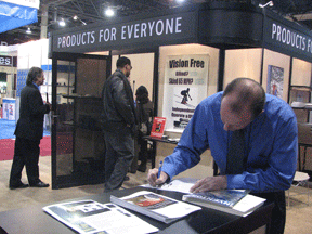 The NFB and Sendero Group jointly sponsored this booth at the Consumer Electronics Showcase in Las Vegas during the first full week of January 2009. Our booth can be seen here with an array of brochures for usable mainstream electronic products. A display lectern is visible on the corner of the table. Several visitors are gathered around the perimeter of the booth to learn about products designed with everyone in mind and to hear our message of universal access.