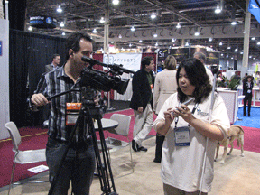 Anne Taylor, NFB director of access technology, shows the Surfboard remote control to Richard Taylor, editor of the BBC program Click. It is an example of an electronic device that is accessible to sighted and blind people alike. Anne is wearing the official Consumer Electronics Showcase T-shirt that all conference exhibitors were asked to wear.