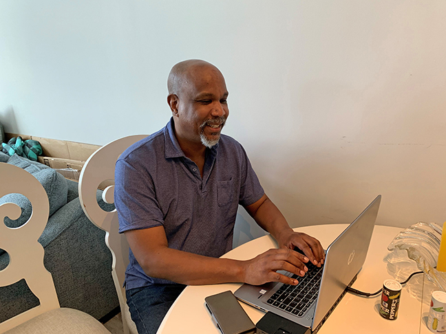 Anil Lewis smiles as he works on his laptop at the dining room table.