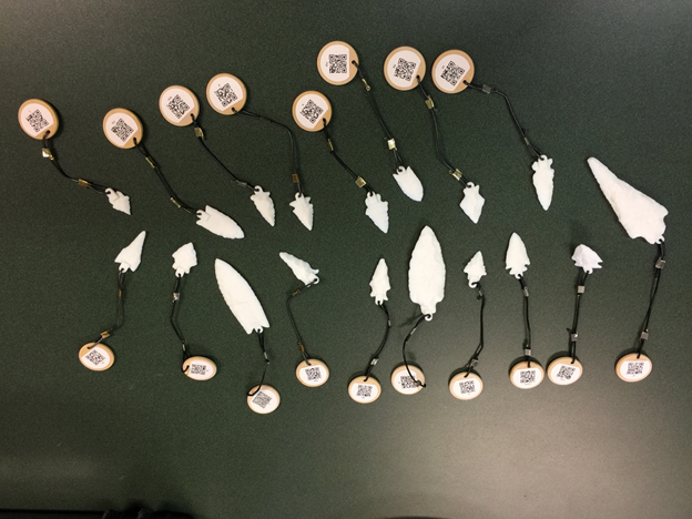 A photograph showing all of the 3D printed points,
with lanyards and wooden coins and QR codes attached to access
additional information.